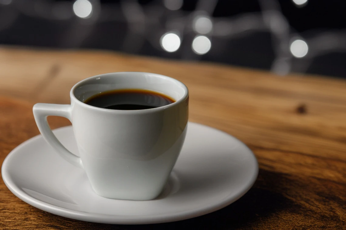 White cup of black coffee on a saucer on a wooden table