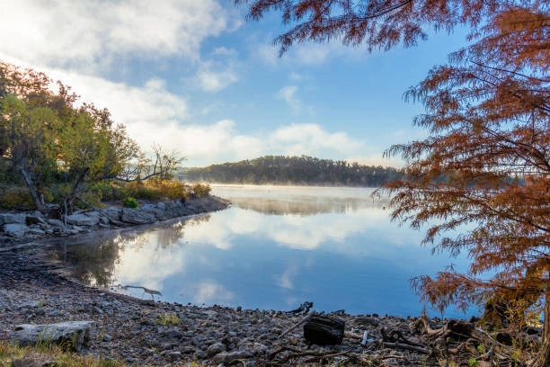 Misty lake shoreline with autumn trees and calm reflections