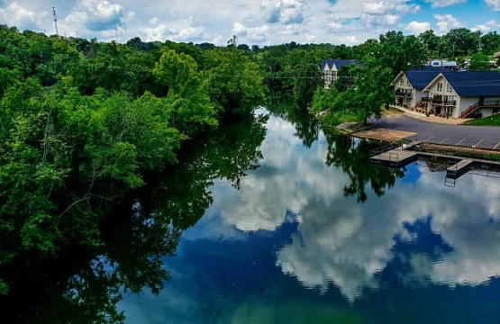 River reflecting clouds and green trees with lakeside lodge and dock