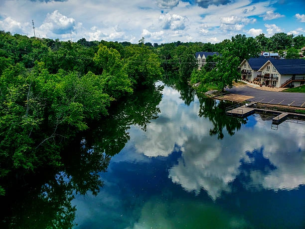 River reflecting clouds and green trees with lakeside lodge and dock
